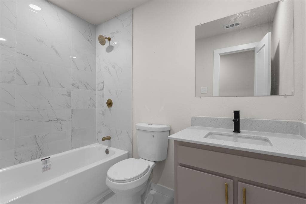 314 NW 15th Street, Grand Prairie, TX 75050 Bathroom featuring a white subway tile surround with brass fixtures, a white bathtub, a toilet, a vanity with a light-toned countertop, and a rectangular mirror