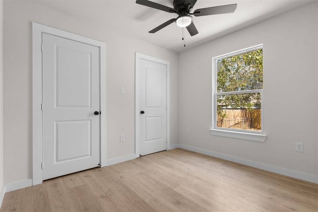 314 NW 15th Street, Grand Prairie, TX 75050 Light-toned wood-finish flooring, white paneled doors with matte black hardware, a window with white trim, and a ceiling fan with integrated lighting