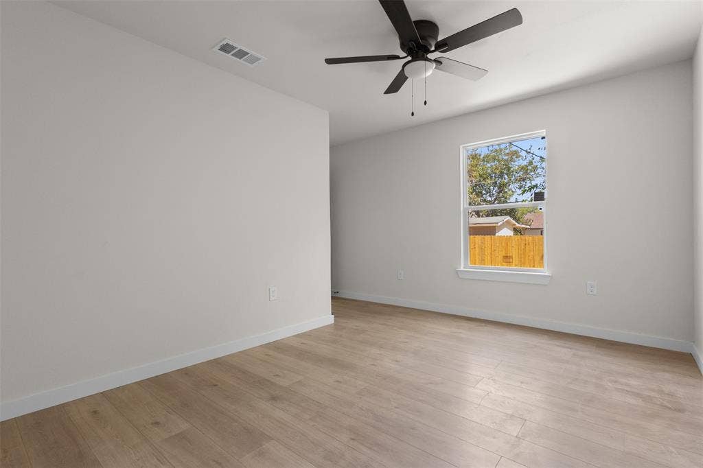314 NW 15th Street, Grand Prairie, TX 75050 Spacious bedroom with wood-finish flooring, ceiling fan with integrated lighting, and natural light from large window framing outdoor landscape views