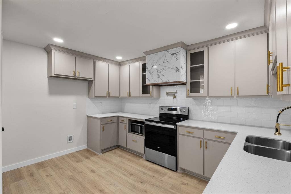314 NW 15th Street, Grand Prairie, TX 75050 Light-toned cabinetry with gold-toned hardware, white subway tile backsplash, light-toned countertops, stainless steel appliances, and wood-finish flooring