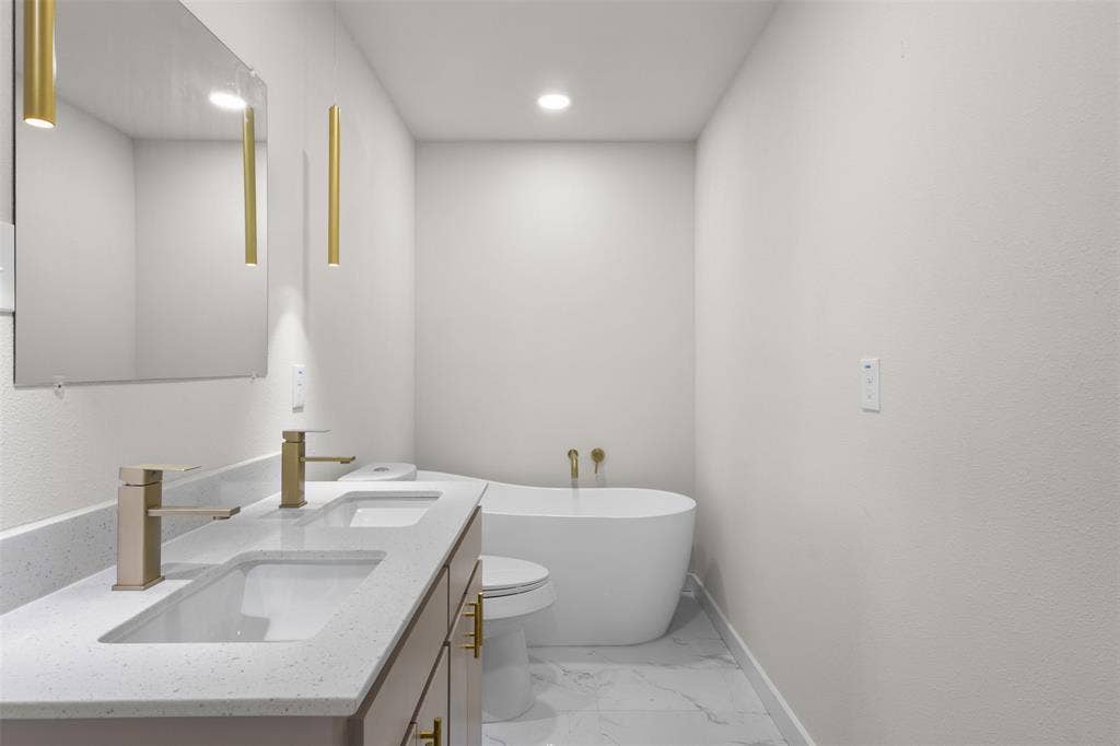 314 NW 15th Street, Grand Prairie, TX 75050 Dual vanity with integrated sinks, freestanding soaking tub, gold-finish fixtures, large wall mirror, and recessed lighting