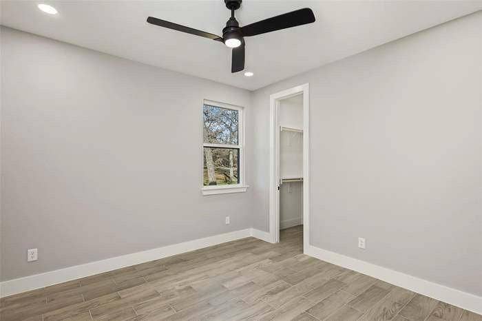 203 Saint Andrews Drive, Mabank, TX 75156 Spacious room featuring wood-finish flooring, a window with exterior tree scenery, a modern ceiling fan with integrated lighting, recessed ceiling lights, and a walk-in closet with built-in shelving