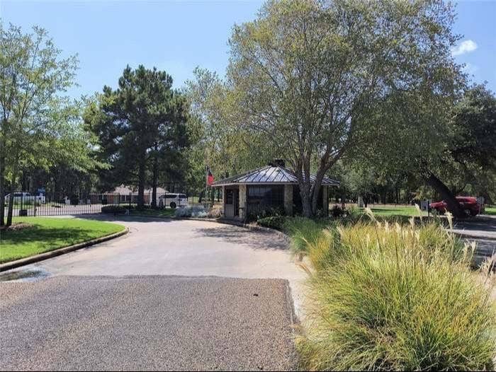 203 Saint Andrews Drive, Mabank, TX 75156 Stone-clad guardhouse with a dark metal roof, featuring a paved entry drive and mature surrounding trees