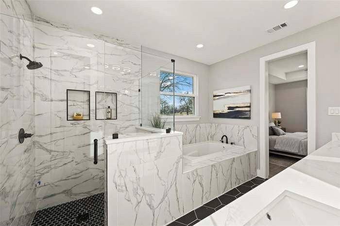 203 Saint Andrews Drive, Mabank, TX 75156 Contemporary bathroom featuring a spacious walk-in shower with black hexagonal floor tiling, a soaking tub with integrated deck, and marble-look wall tiling
