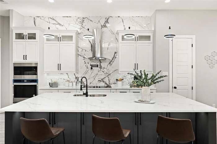 203 Saint Andrews Drive, Mabank, TX 75156 Gourmet kitchen featuring a large central island with seating, white shaker cabinetry, a full height marble-look backsplash, stainless steel appliances, and modern pendant lighting