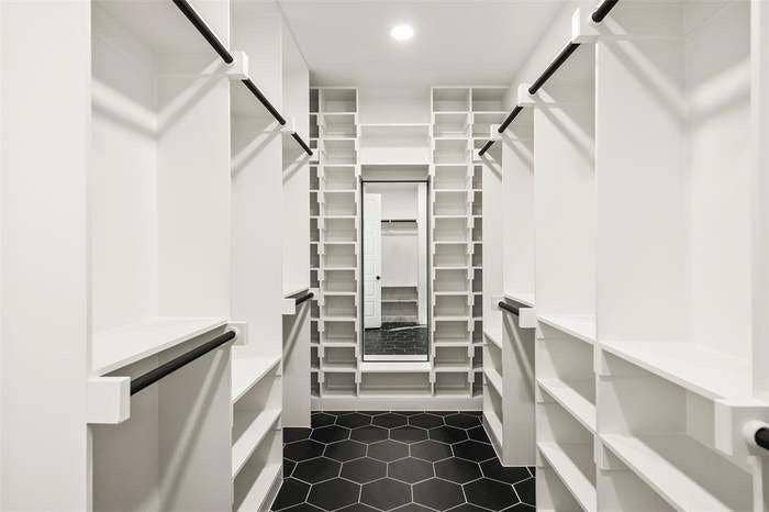 203 Saint Andrews Drive, Mabank, TX 75156 Walk-in closet featuring extensive built-in shelving, multiple hanging rods, black hexagonal floor tiling, and a full-length mirror
