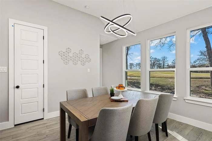203 Saint Andrews Drive, Mabank, TX 75156 Dining area featuring three large windows, a contemporary linear chandelier, gray wall paint, and wood-finish flooring