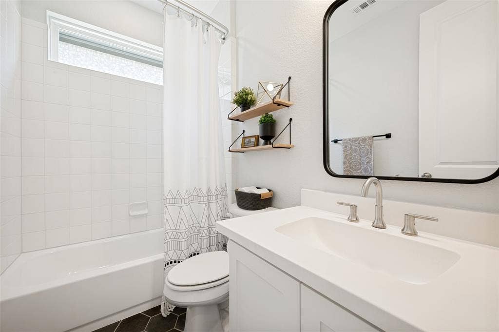 961 Gladewater Drive, Prosper, TX 75078 This bright bathroom has a shower/tub combo and modern white aesthetic with trendy dark tile flooring
