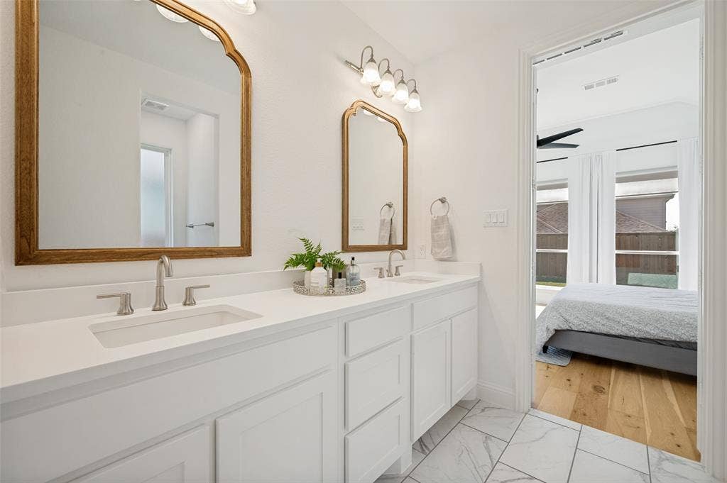 961 Gladewater Drive, Prosper, TX 75078 Modern white counters and cabinets create a visual contrast to the light wood accent mirrors giving this primary bathroom a soft, spa like atmosphere