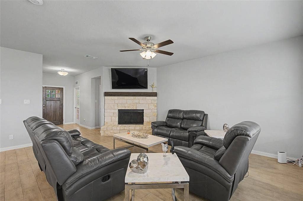 185 Chester Road, Springtown, TX 76082 Living area featuring wood-finish flooring, a stone-clad fireplace with a wood mantel, a ceiling fan with integrated lighting, and neutral wall tones