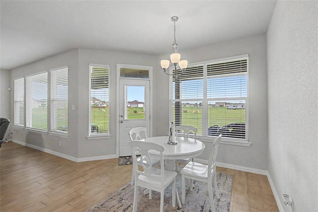 185 Chester Road, Springtown, TX 76082 Dining area featuring wood-finish flooring, light gray walls, multiple windows with blinds, a white exterior door with a transom window, and a chandelier