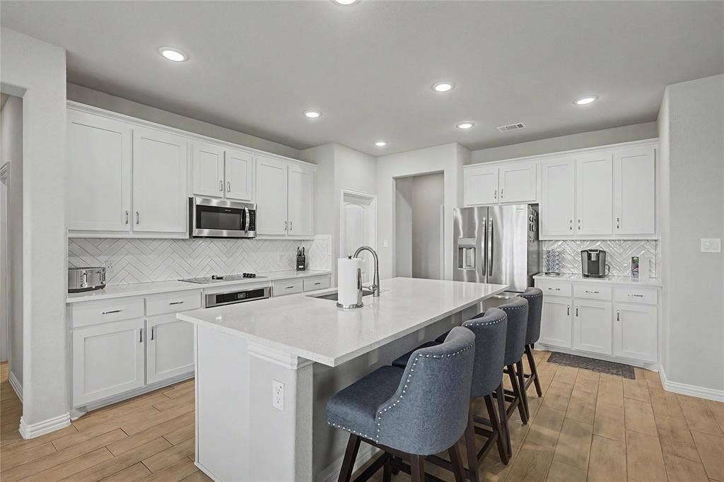 185 Chester Road, Springtown, TX 76082 Kitchen featuring light wood-finish flooring, white cabinetry, integrated stainless steel appliances, a herringbone tile backsplash, and a large central island with a solid surface countertop