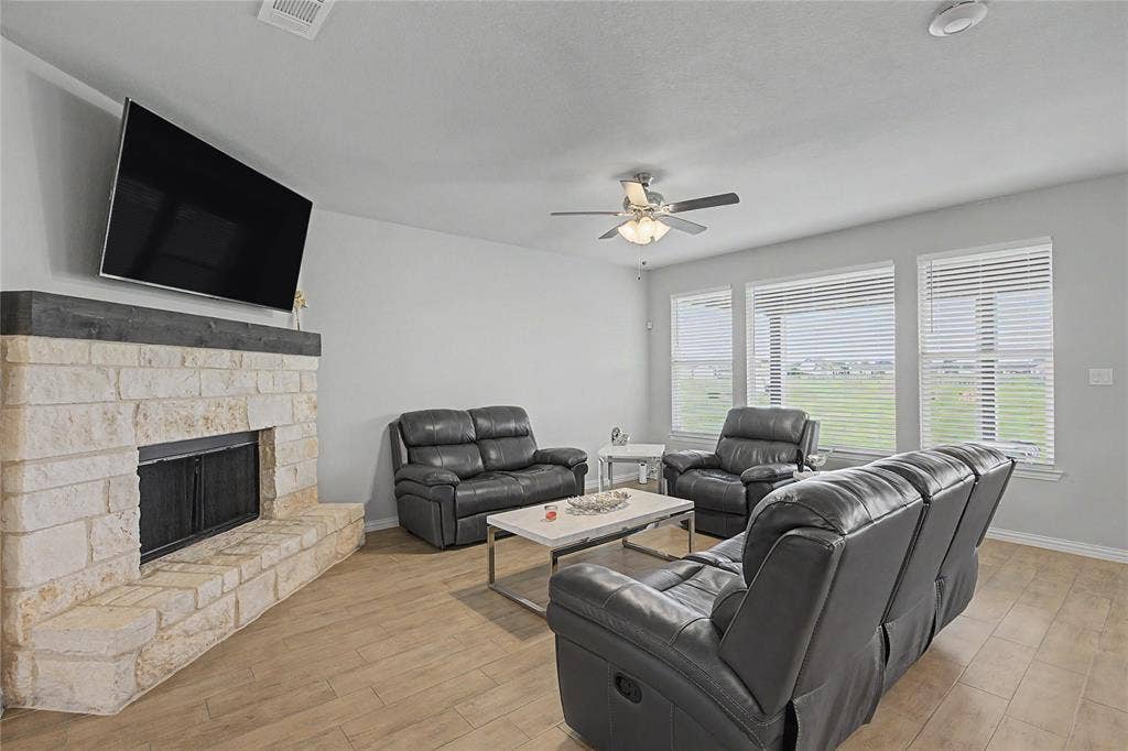 185 Chester Road, Springtown, TX 76082 Living area featuring a stone-faced fireplace with a dark wood-finish mantel, wood-finish flooring, and multiple windows with blinds