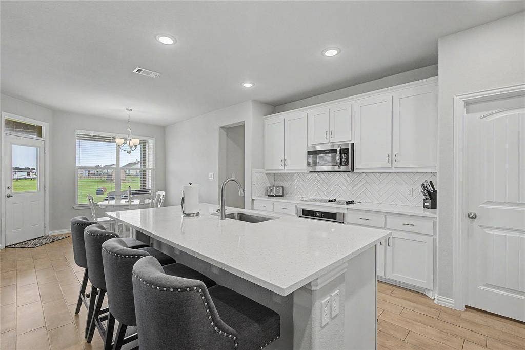 185 Chester Road, Springtown, TX 76082 Spacious kitchen featuring a large island with sink, quartz countertops, white shaker cabinetry, stainless steel appliances, and a herringbone tile backsplash