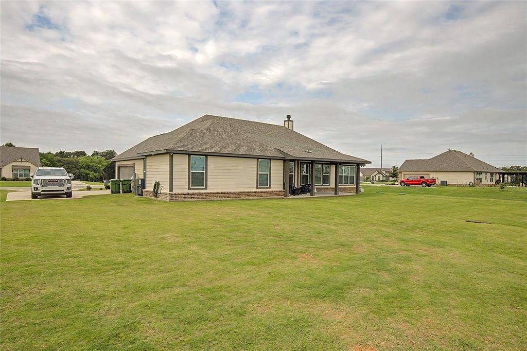 185 Chester Road, Springtown, TX 76082 Expansive green lawn surrounds the property, featuring a covered patio with dark posts, multiple windows, and a side-entry garage