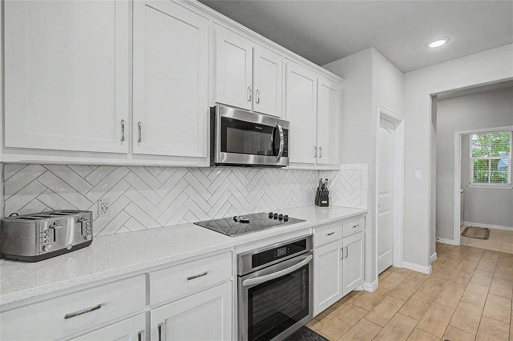185 Chester Road, Springtown, TX 76082 Modern kitchen featuring white shaker cabinetry, stainless steel appliances, a white herringbone tile backsplash, and light-toned countertops