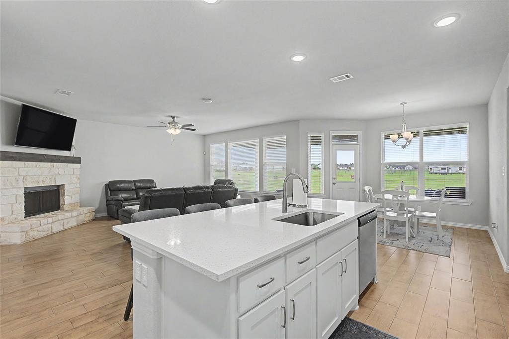 185 Chester Road, Springtown, TX 76082 Expansive kitchen island with a white countertop and undermount sink, stainless steel dishwasher, wood-finish flooring, stone fireplace, and ample natural light from multiple windows