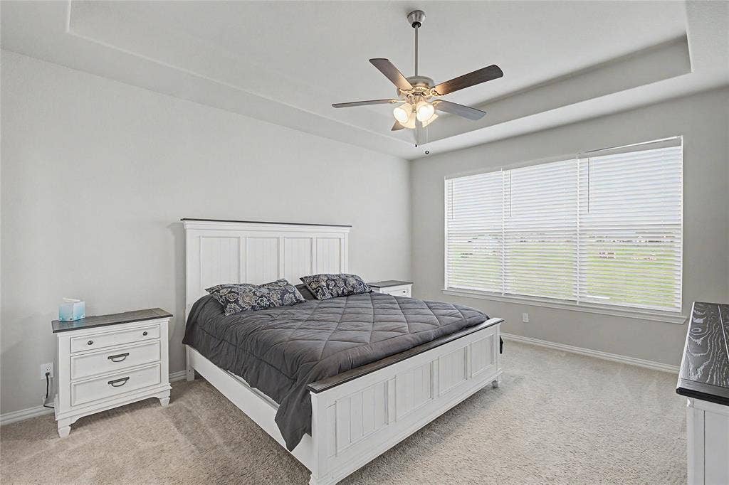 185 Chester Road, Springtown, TX 76082 Spacious room featuring a tray ceiling, ceiling fan with integrated lighting, expansive window with horizontal blinds, and neutral carpeting