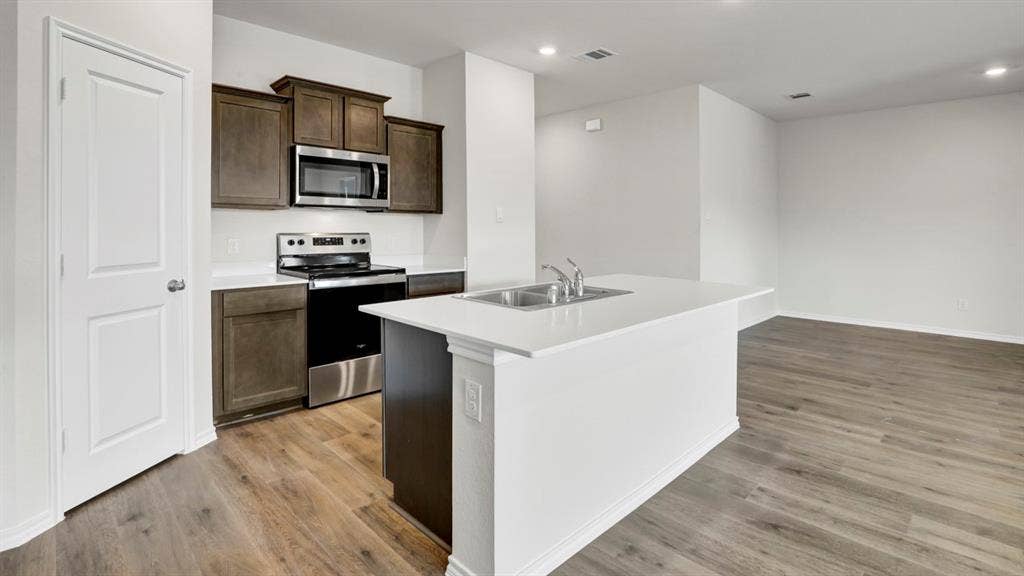 200 Bandit Trail, Terrell, TX 75160 Modern kitchen featuring a central island with a double basin sink, white countertops, stainless steel appliances, dark wood-finish cabinetry, and wood-finish flooring