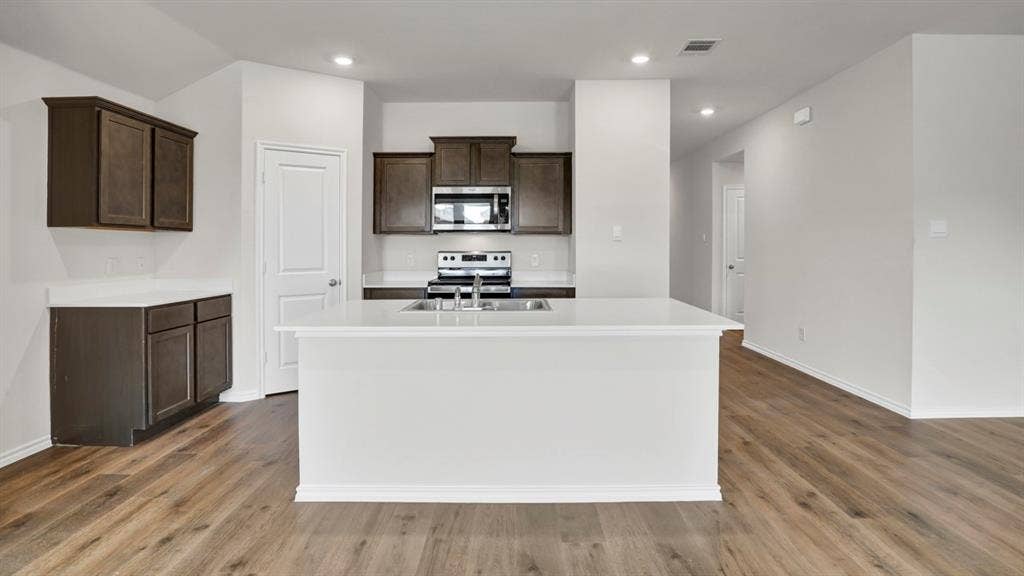 200 Bandit Trail, Terrell, TX 75160 Open-concept kitchen featuring an expansive center island, dark wood-finish cabinetry, bright white countertops, stainless steel appliances, and wood-finish flooring