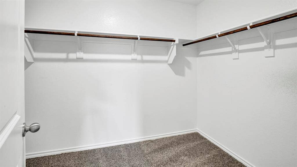 200 Bandit Trail, Terrell, TX 75160 Walk-in closet featuring white walls, gray carpet, and two levels of wood-finish hanging rods with shelving