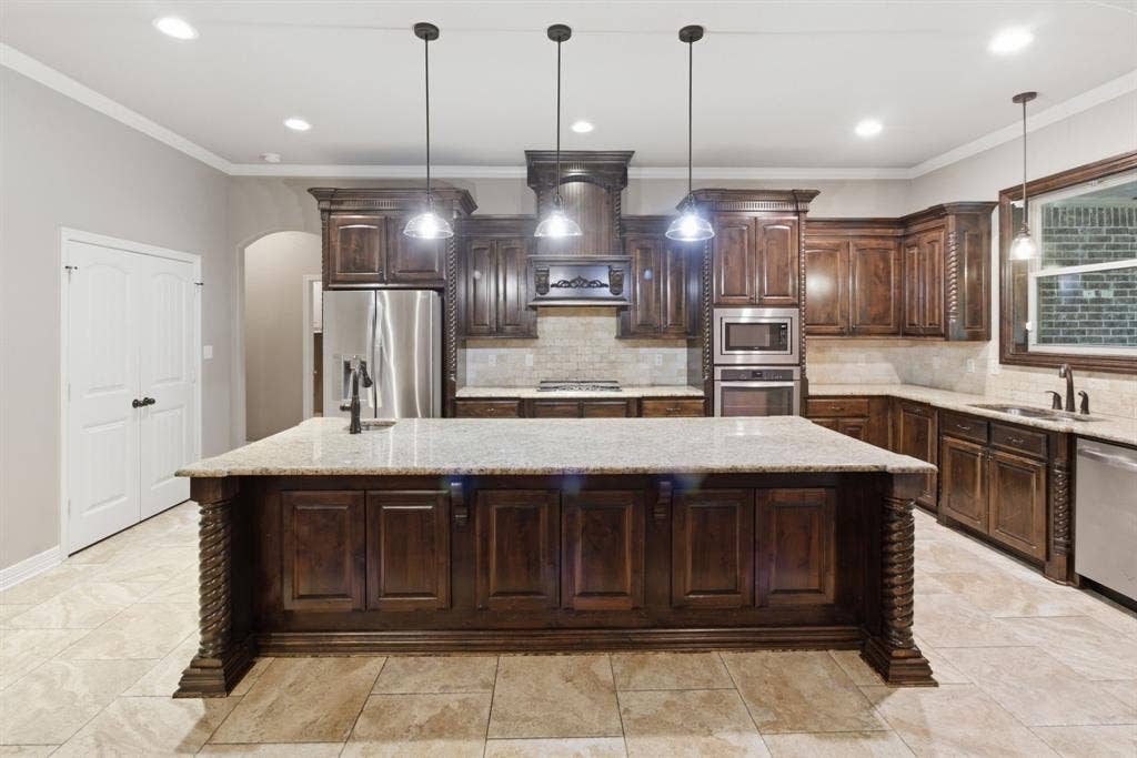 7765 Hickory Spring Lane, Tyler, TX 75703 Kitchen featuring a large central island with pendant lighting, rich wood cabinetry, stainless steel appliances, light-colored countertops, and a complementary tile backsplash