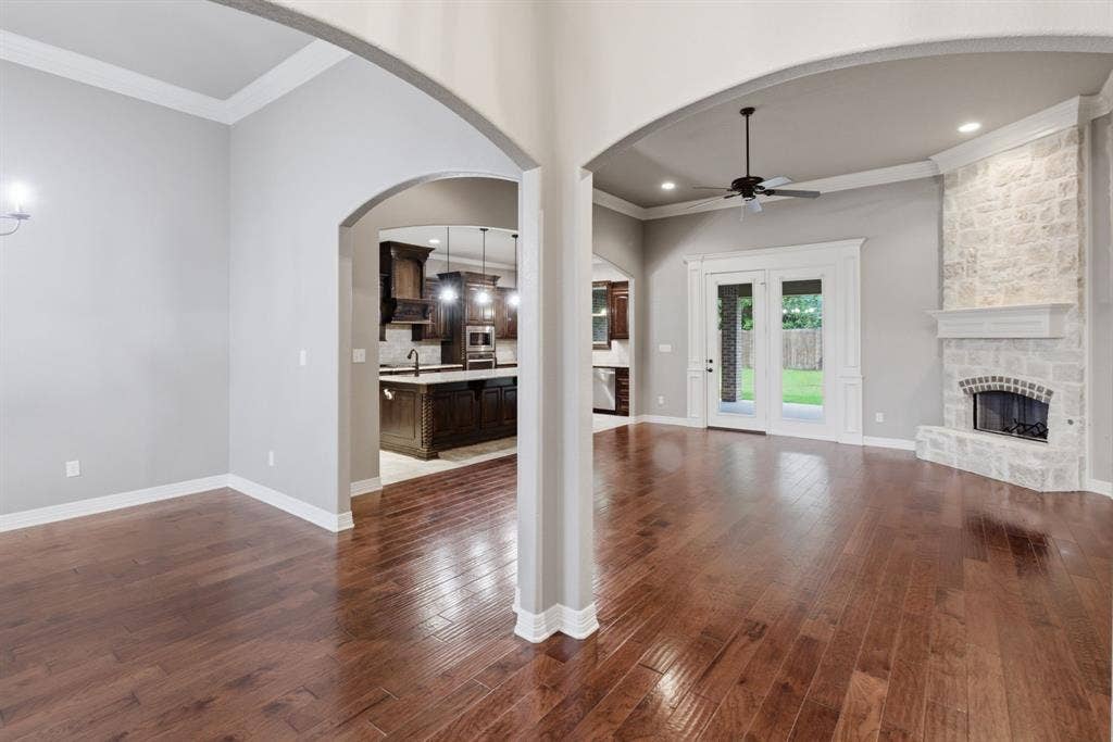 7765 Hickory Spring Lane, Tyler, TX 75703 Spacious room featuring rich wood-finish flooring, a stone-clad fireplace with a hearth, double French doors leading to exterior space, and an arched entryway