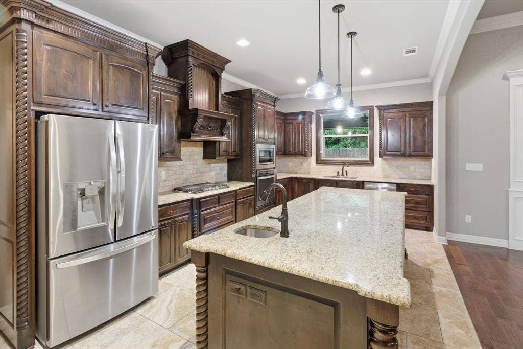 7765 Hickory Spring Lane, Tyler, TX 75703 Gourmet kitchen featuring a large central island with granite countertop, stainless steel appliances, dark wood cabinetry with decorative molding, and tile flooring