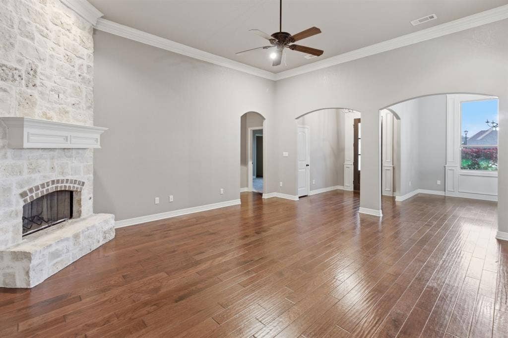 7765 Hickory Spring Lane, Tyler, TX 75703 Spacious living area featuring a stone-clad fireplace with mantel, hardwood flooring, arched doorways, crown molding, and a ceiling fan