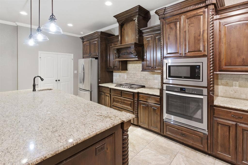 7765 Hickory Spring Lane, Tyler, TX 75703 Kitchen featuring dark wood cabinetry with decorative rope trim, light granite countertops, stainless steel appliances including a built-in oven and microwave, and a tile backsplash