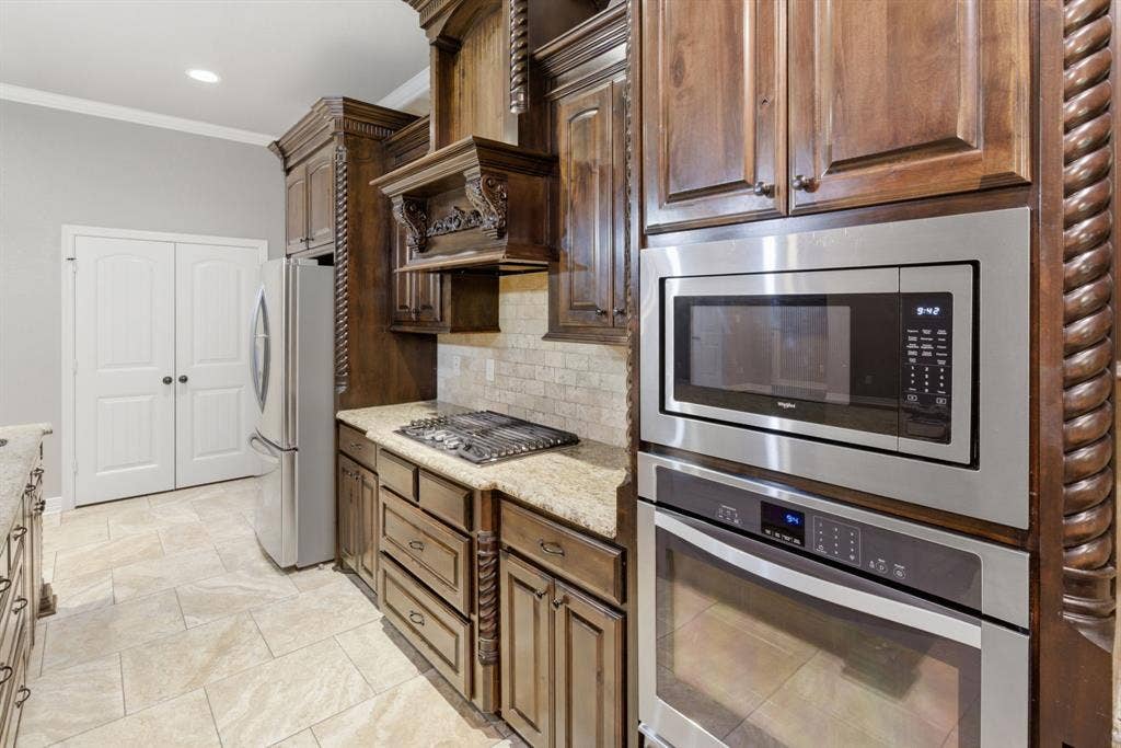 7765 Hickory Spring Lane, Tyler, TX 75703 Kitchen featuring rich wood cabinetry, granite countertops, tile backsplash, and stainless steel appliances including a built-in microwave, wall oven, and gas cooktop