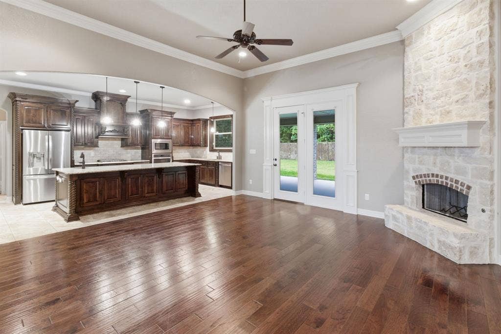 7765 Hickory Spring Lane, Tyler, TX 75703 Open-concept living area featuring rich wood-finish flooring, a stone fireplace with a white mantel, and glass double doors opening to the exterior