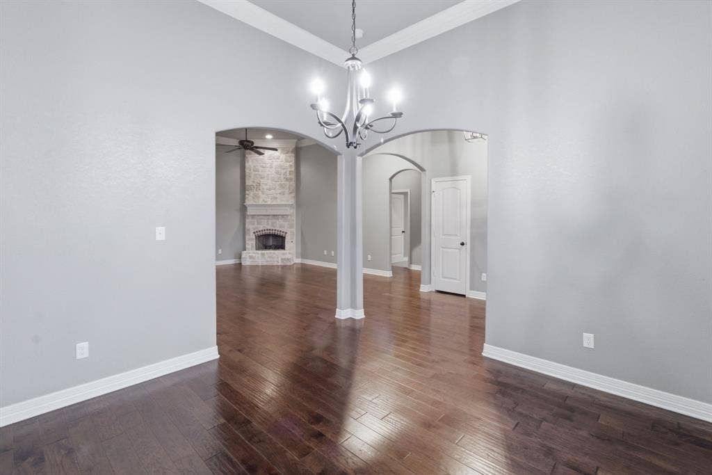 7765 Hickory Spring Lane, Tyler, TX 75703 Hardwood-finish flooring throughout, featuring a chandelier lighting fixture, arched doorways, and a stone-clad fireplace