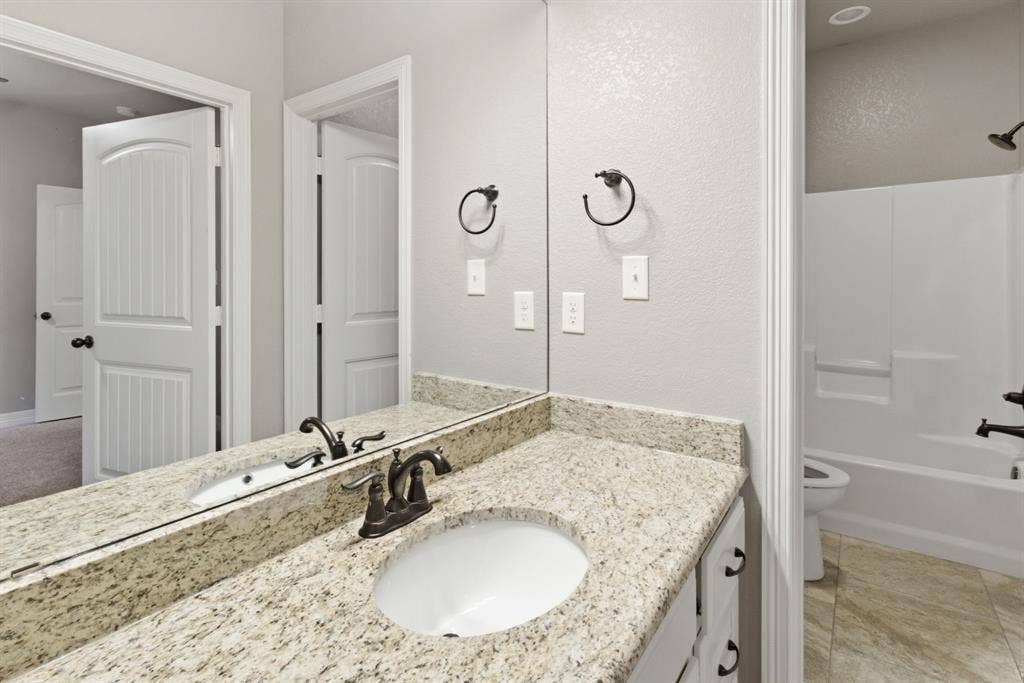 7765 Hickory Spring Lane, Tyler, TX 75703 Bathroom vanity featuring an integrated sink, bronze-finish faucet, and speckled countertop