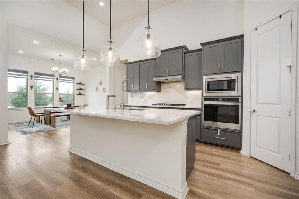 2813 Walker Way, Northlake, TX 76247 Modern kitchen featuring a large central island with a waterfall countertop, gray cabinetry, built-in stainless steel appliances, and wood-finish flooring