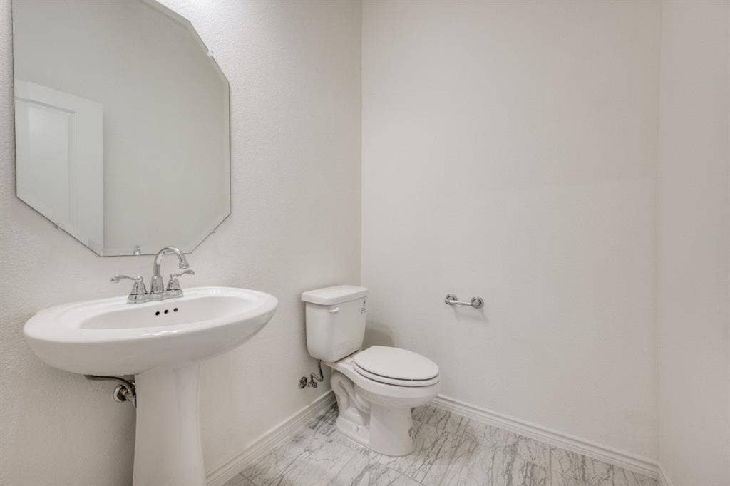 2813 Walker Way, Northlake, TX 76247 White pedestal sink with chrome faucet, octagonal wall mirror, and a white toilet