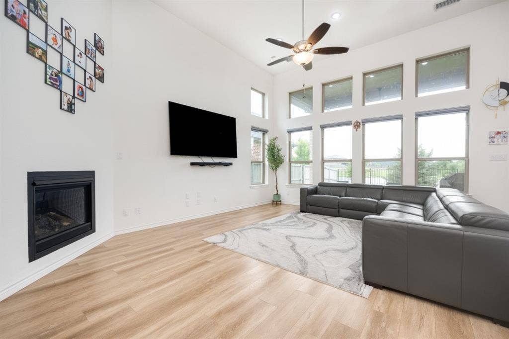 2813 Walker Way, Northlake, TX 76247 Vaulted ceiling living area featuring a built-in fireplace, wood-finish flooring, a ceiling fan with integrated lighting, and multiple large windows