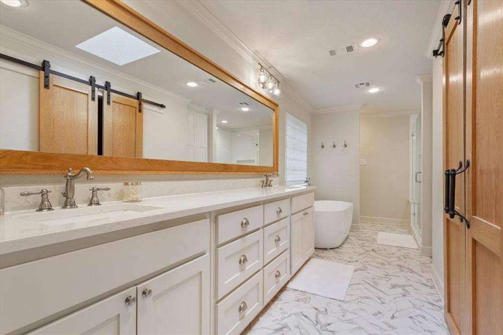 402 Shadow Mountain Drive, Woodway, TX 76712 Upstairs bathroom featuring a dual vanity with white cabinetry and light-colored countertops, a freestanding soaking tub, and a glass-enclosed shower