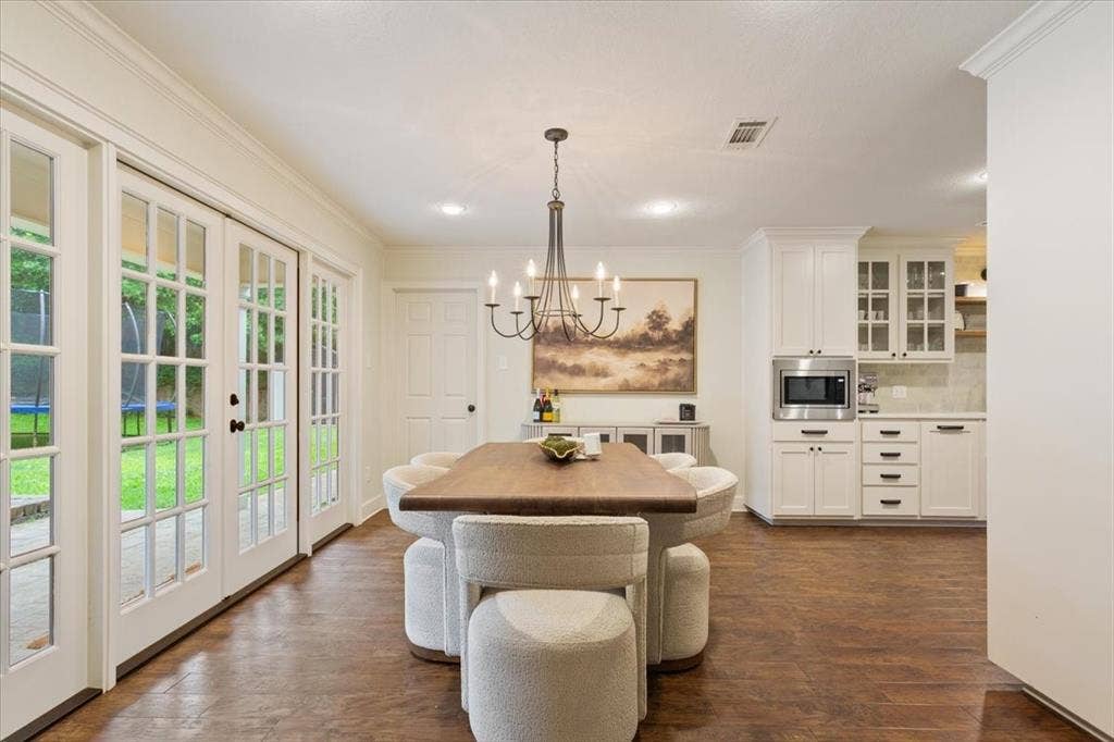 402 Shadow Mountain Drive, Woodway, TX 76712 Dining area featuring wood-finish flooring, two sets of French patio doors, and an adjacent built-in serving area with white cabinetry and a built-in microwave