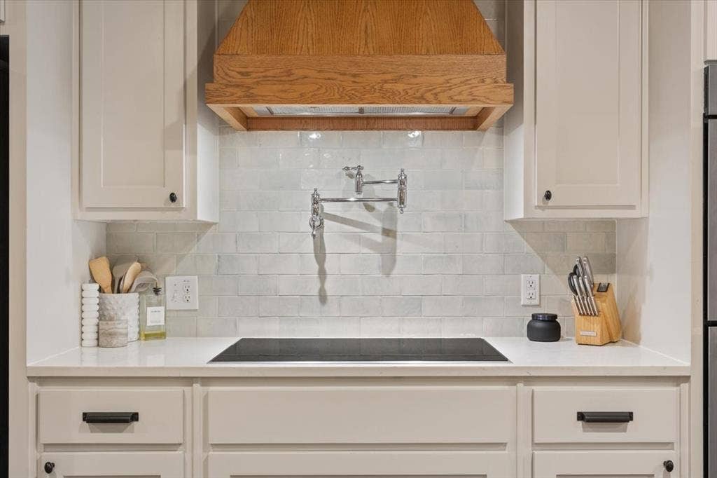 402 Shadow Mountain Drive, Woodway, TX 76712 Induction cooktop with an integrated pot filler, surrounded by a light-colored subway tile backsplash and a custom wood range hood
