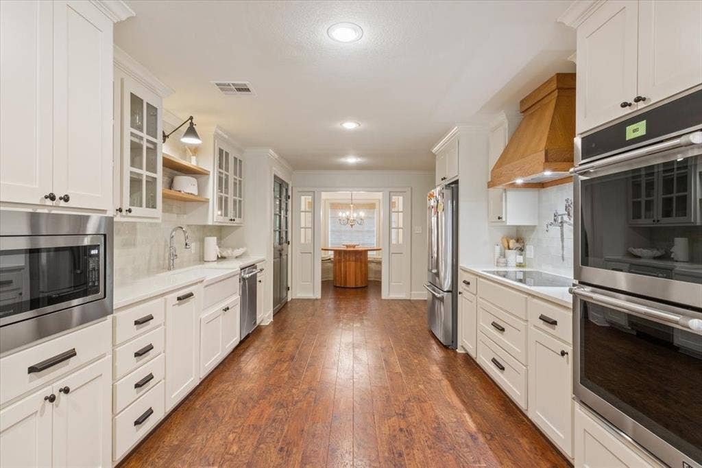 402 Shadow Mountain Drive, Woodway, TX 76712 Expansive kitchen featuring wood-finish flooring, white cabinetry with dark hardware, stainless steel appliances, and a wood range hood
