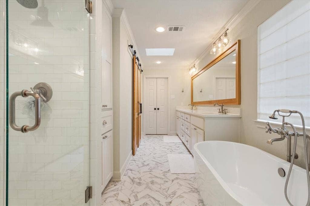 402 Shadow Mountain Drive, Woodway, TX 76712 Upstairs freestanding soaking tub with floor-mounted fixture, dual vanity with undermount sinks, and a large framed mirror with overhead lighting
