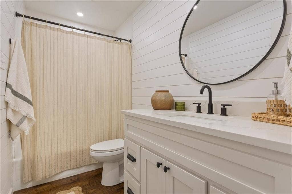 402 Shadow Mountain Drive, Woodway, TX 76712 Upstairs bathroom featuring a single vanity with a white countertop, matte black fixtures, an oval mirror, and horizontal shiplap wall paneling
