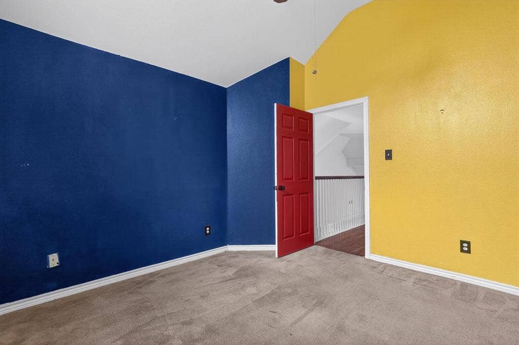 Carpeted room featuring a red six-panel door, white trim, and a vaulted ceiling