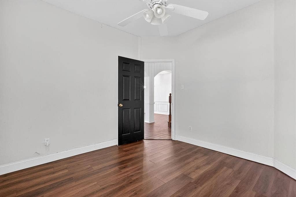 Room featuring wood-finish flooring, white walls, and a ceiling fan with light fixture
