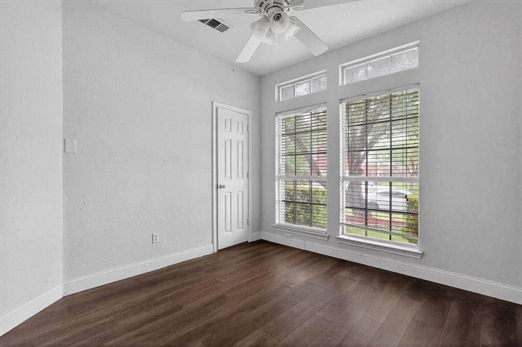Spacious room featuring wood-finish flooring, white baseboards, and a white paneled door