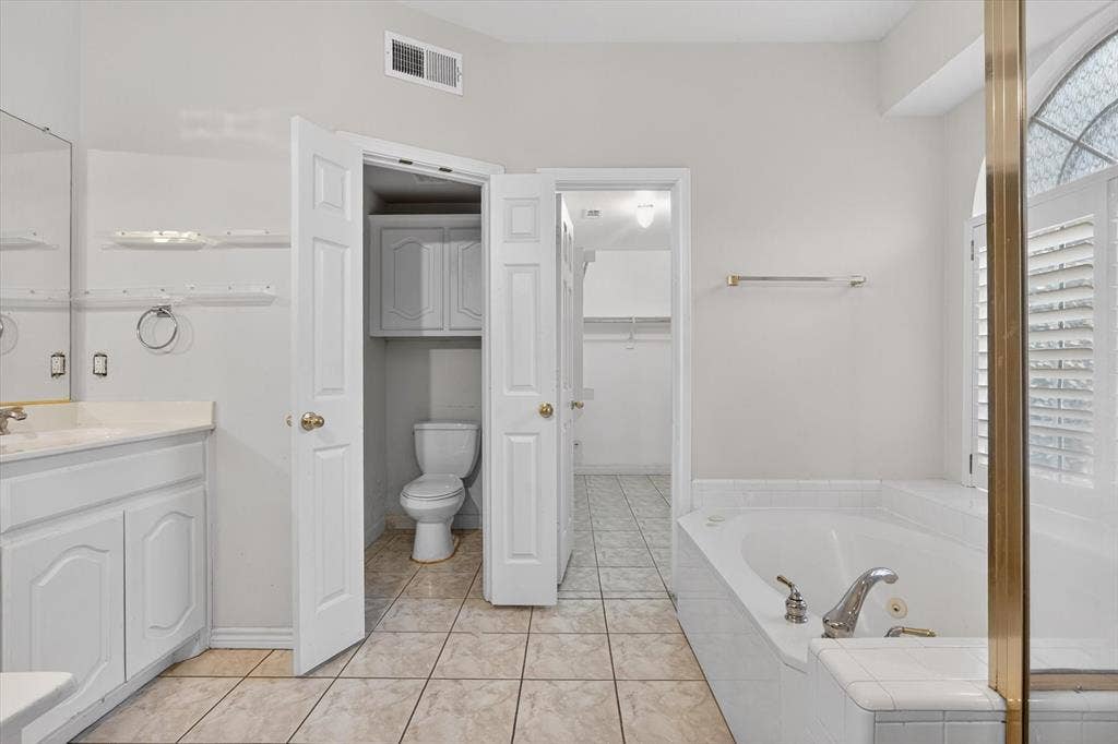 Bathroom featuring a built-in tub with tile surround, a single vanity with stone-finish countertop, and a water closet with built-in cabinetry