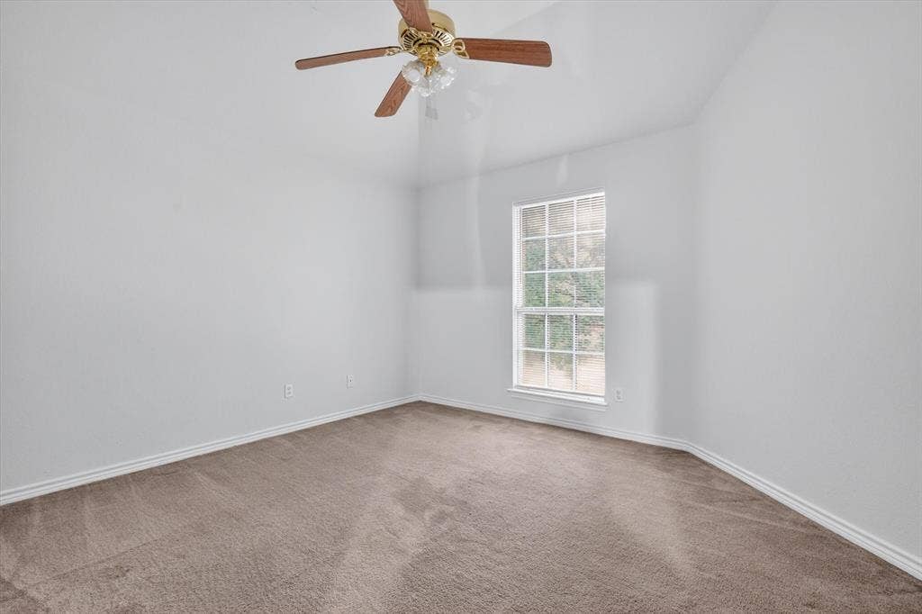 Carpeted interior space featuring a single window with grids, white trim, and a ceiling fan