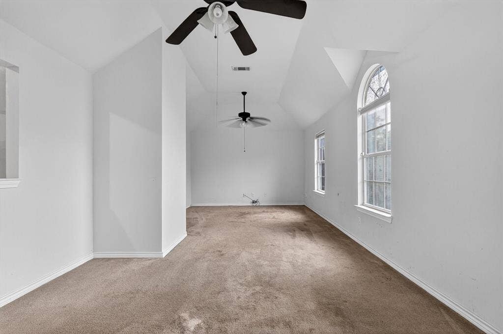 Spacious room featuring a vaulted ceiling and two ceiling fans