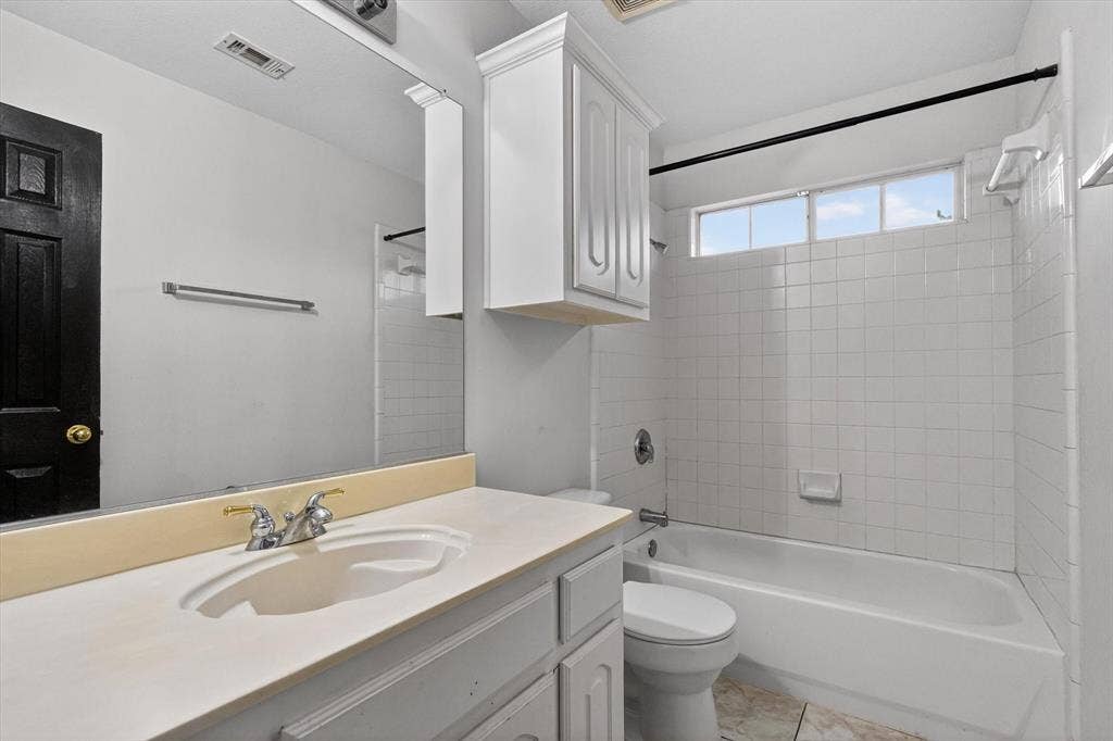 Bathroom featuring a vanity with an integrated sink, a white bathtub with tile surround, and a high transom window